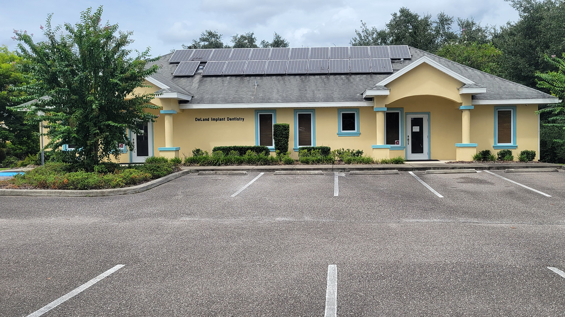 The image shows a small, yellow building with a blue roof and white trim, featuring a sign that reads The Medical Center. There is a parking lot in front of the building with several empty spaces. The sky is overcast, suggesting it might be a cloudy day.