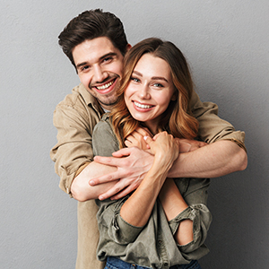 A young couple embracing warmly, with the man in a brown shirt and the woman in a blue top.