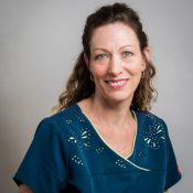 The image is a portrait of a woman wearing a blue scrub top and smiling at the camera.