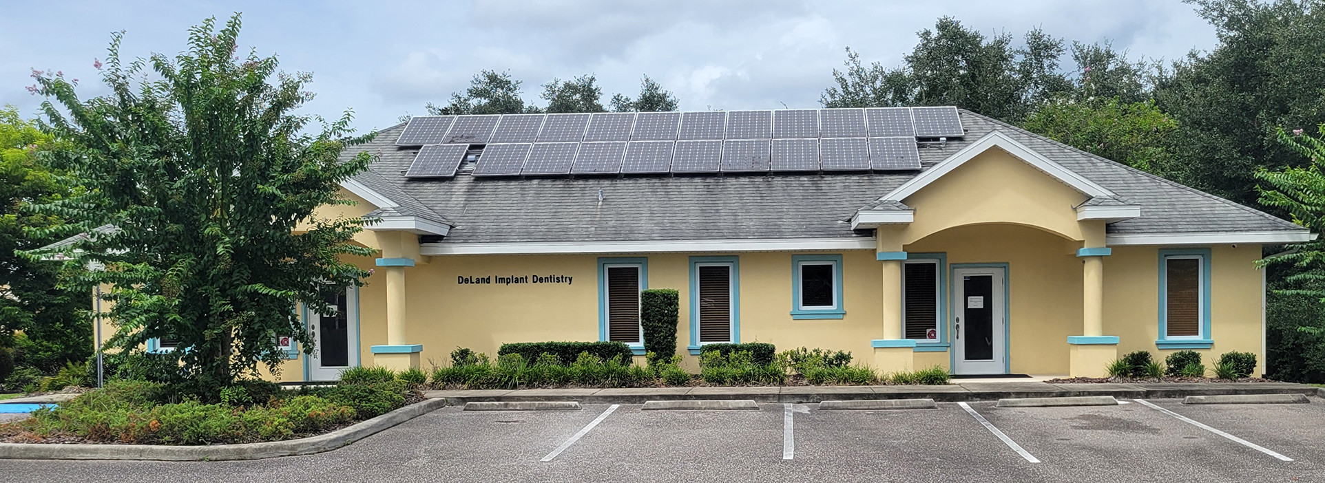 A two-story building with a yellow exterior, featuring a solar panel on the roof and a parking lot in front.