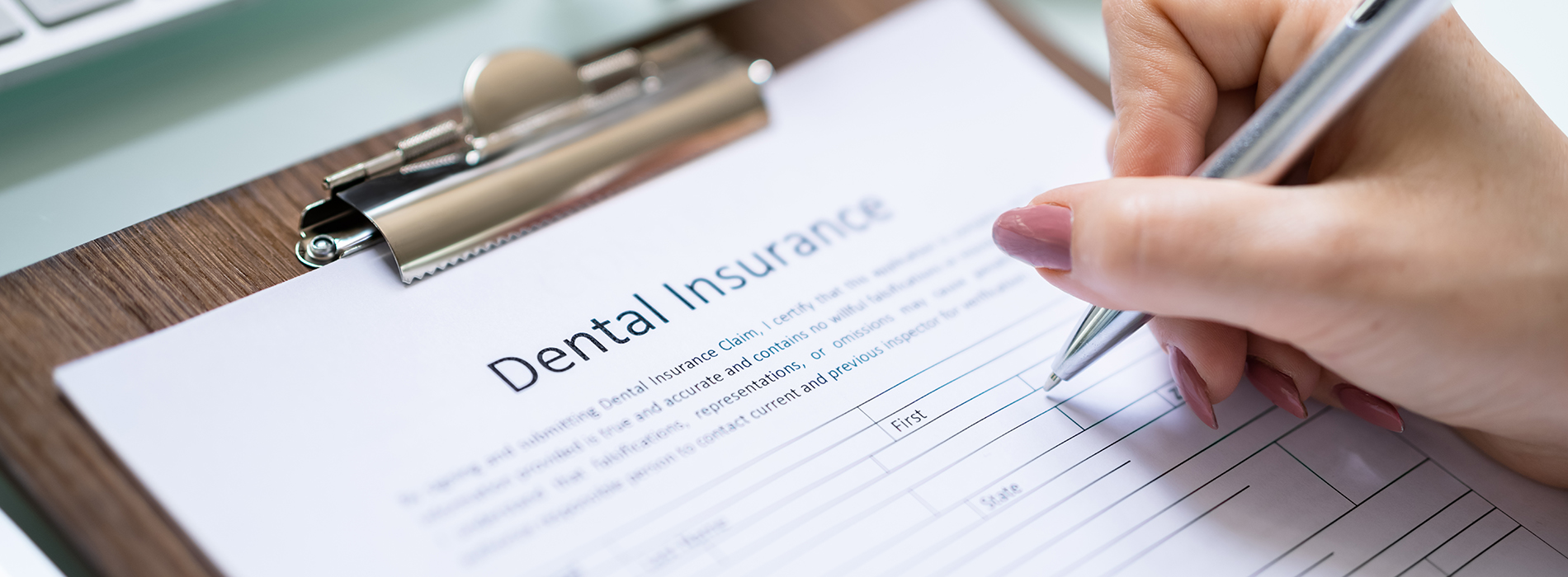 A person s hand holding a pen above a clipboard with a form titled  Dental Insurance , displaying the words  Insurance Information  and  Dentist .