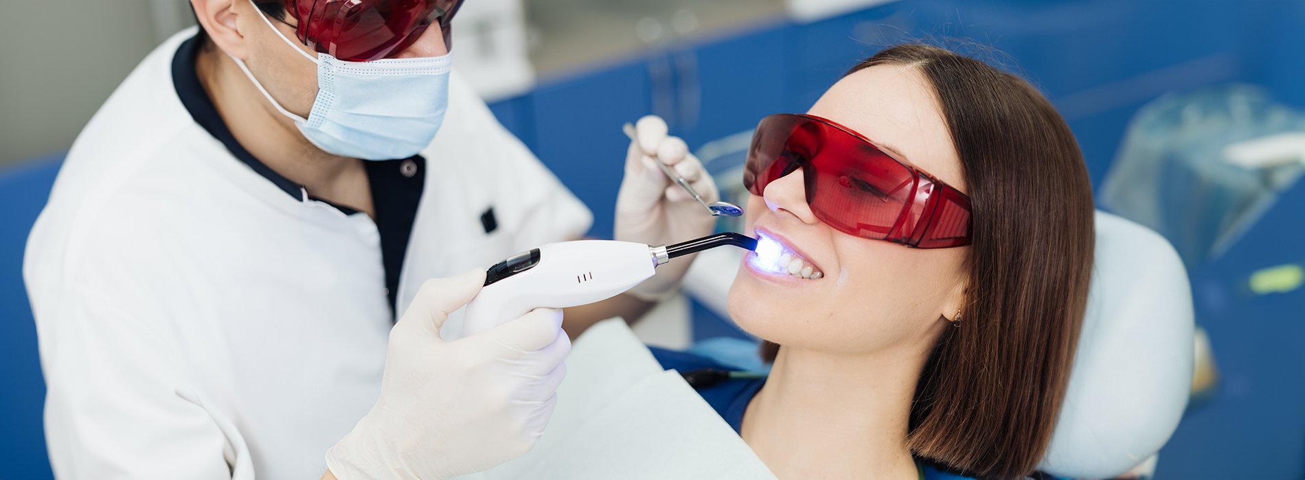 The image shows a dental professional performing a tooth cleaning procedure on a patient in a dental office setting.