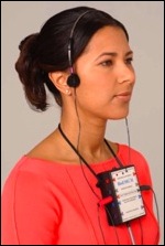 Woman wearing a headset with multiple earpieces, standing in front of a pink background.