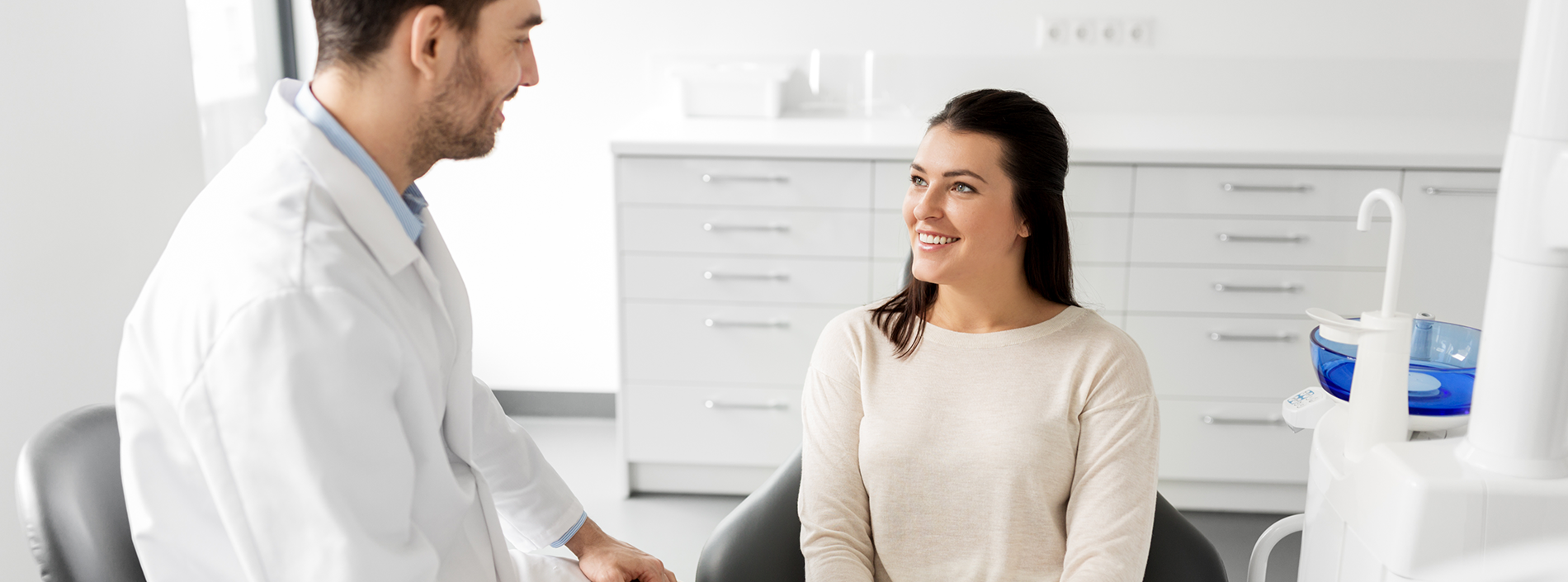 A dentist in a white coat is attending to a patient sitting in a dental chair.