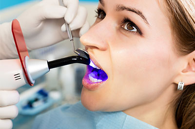 An image of a woman receiving dental care, with her mouth open and a dental device inserted, under the supervision of a dental professional.