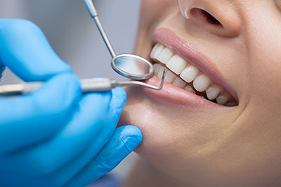 A dental hygienist is performing a cleaning procedure on a patient s teeth, with the patient smiling and wearing a blue surgical gown.