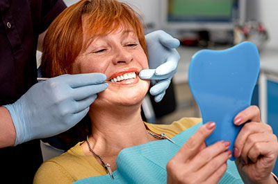 A woman in a dental chair, receiving dental care, with a dental professional and tools visible.