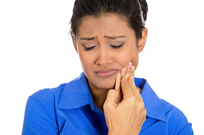 A woman with a concerned expression, holding her finger to her mouth, possibly in the act of brushing or examining her teeth.