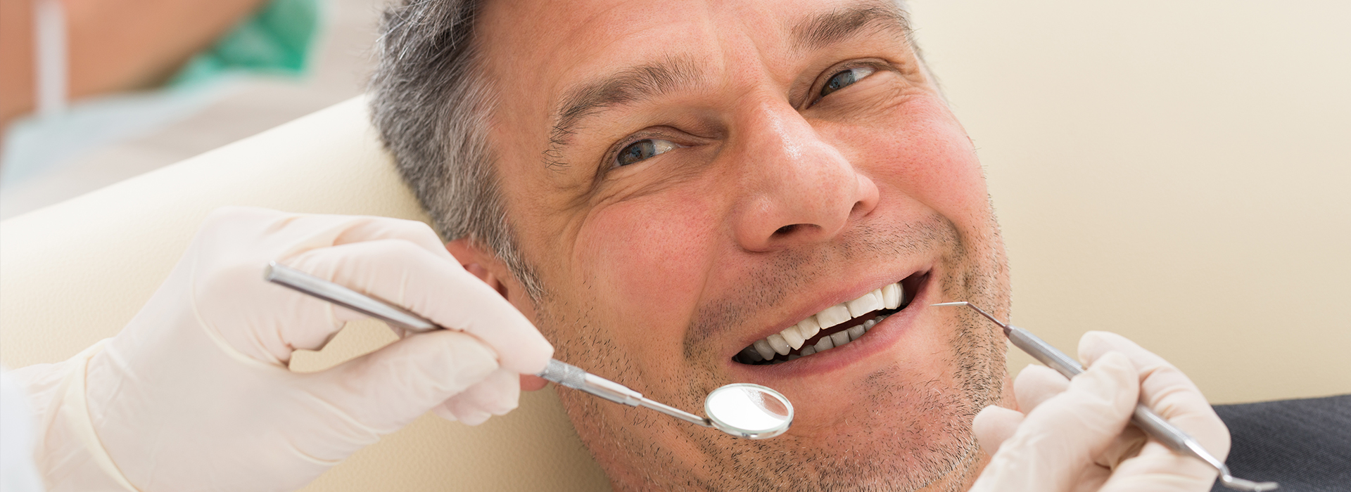 A smiling man in a dental chair receiving a dental treatment, with a dentist working on his teeth using dental tools.