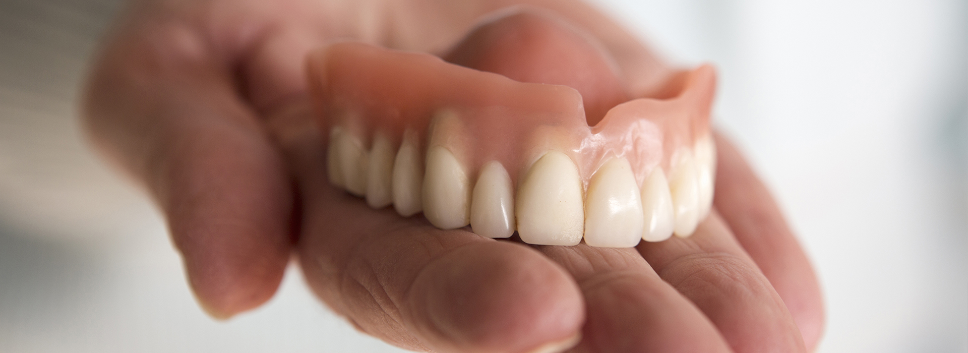 A person holding a set of dentures with a toothy smile.