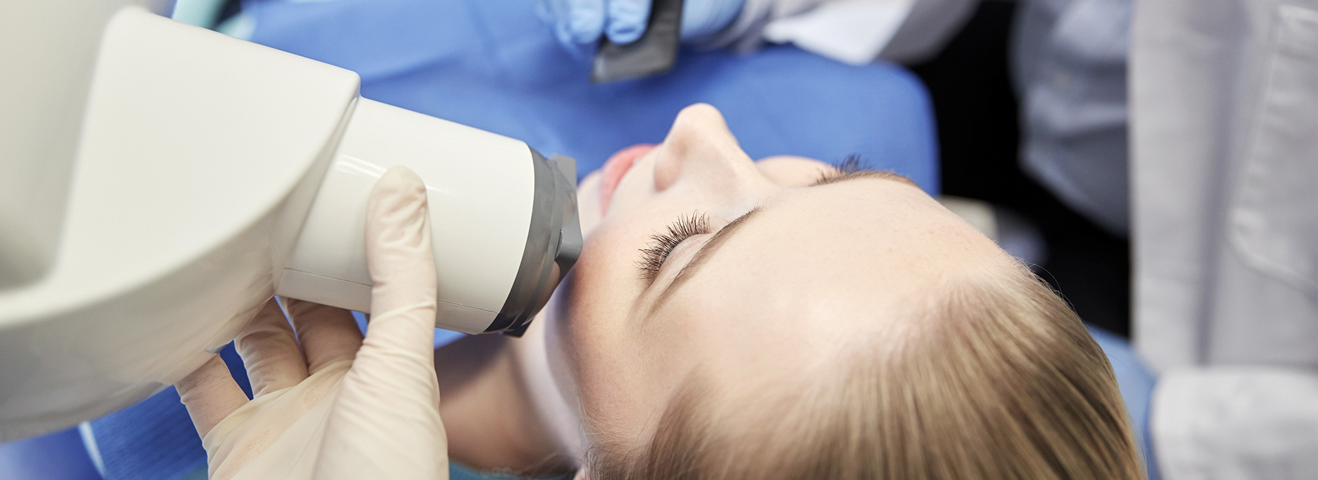 A person receiving a facial treatment, likely at a medical or beauty facility, with a device held by a professional.