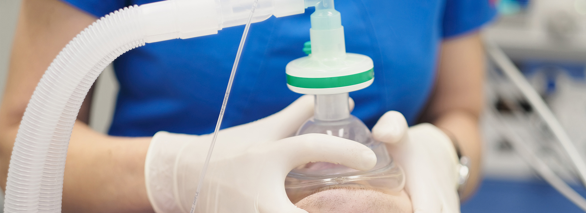 Woman in white gloves holding a clear plastic tube connected to a green cap, which appears to be part of medical equipment.