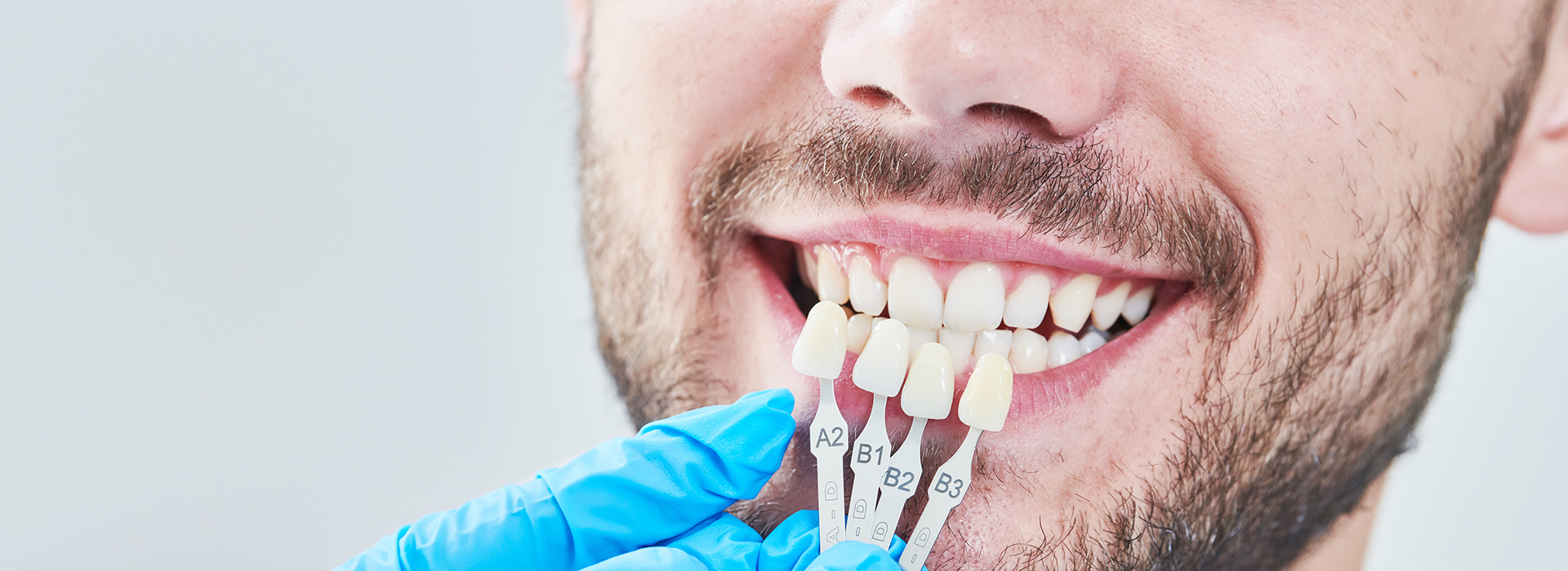 The image shows a man smiling, with a focus on his teeth being worked on by a dental professional using a drill and other tools.