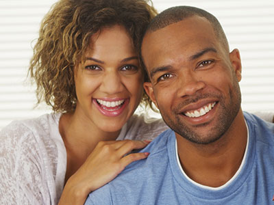 A smiling couple posing for a photo, with the man on the left and the woman on the right.