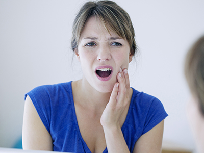 A woman with her mouth open, showing concern or discomfort while looking at her reflection in the mirror.