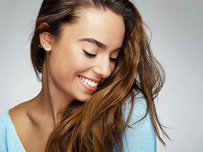 A young woman with long brown hair and a radiant smile, looking over her shoulder.