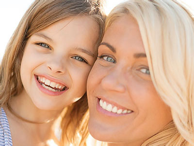 A woman and a child smiling at the camera, with the woman s face partially obscured by the child.