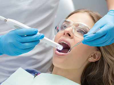 A dental professional using a device to clean a woman s teeth in a clinical setting.