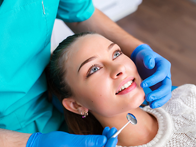 The image shows a person sitting in a dental chair, receiving dental care from a professional wearing blue gloves and a stethoscope.