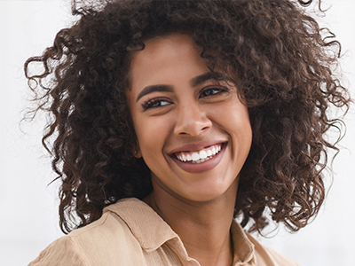 The image features a smiling individual with curly hair, wearing a light-colored top and a warm expression.